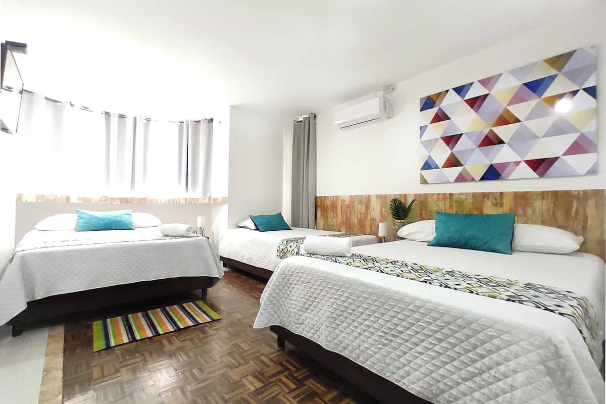 A hotel room with two beds, a wooden floor, a colorful geometric wall art, and an air conditioning unit.