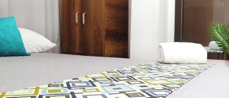 A hotel room with a bed, a wooden wardrobe, a mirror, and a patterned rug.