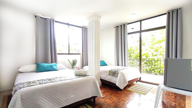 A hotel room with two beds, a window with curtains, a wooden floor, and a view of greenery outside. - Walena Hotel (Riohacha)