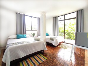 A hotel room with two beds, a window with curtains, a wooden floor, and a view of greenery outside. - Walena Hotel (Riohacha)