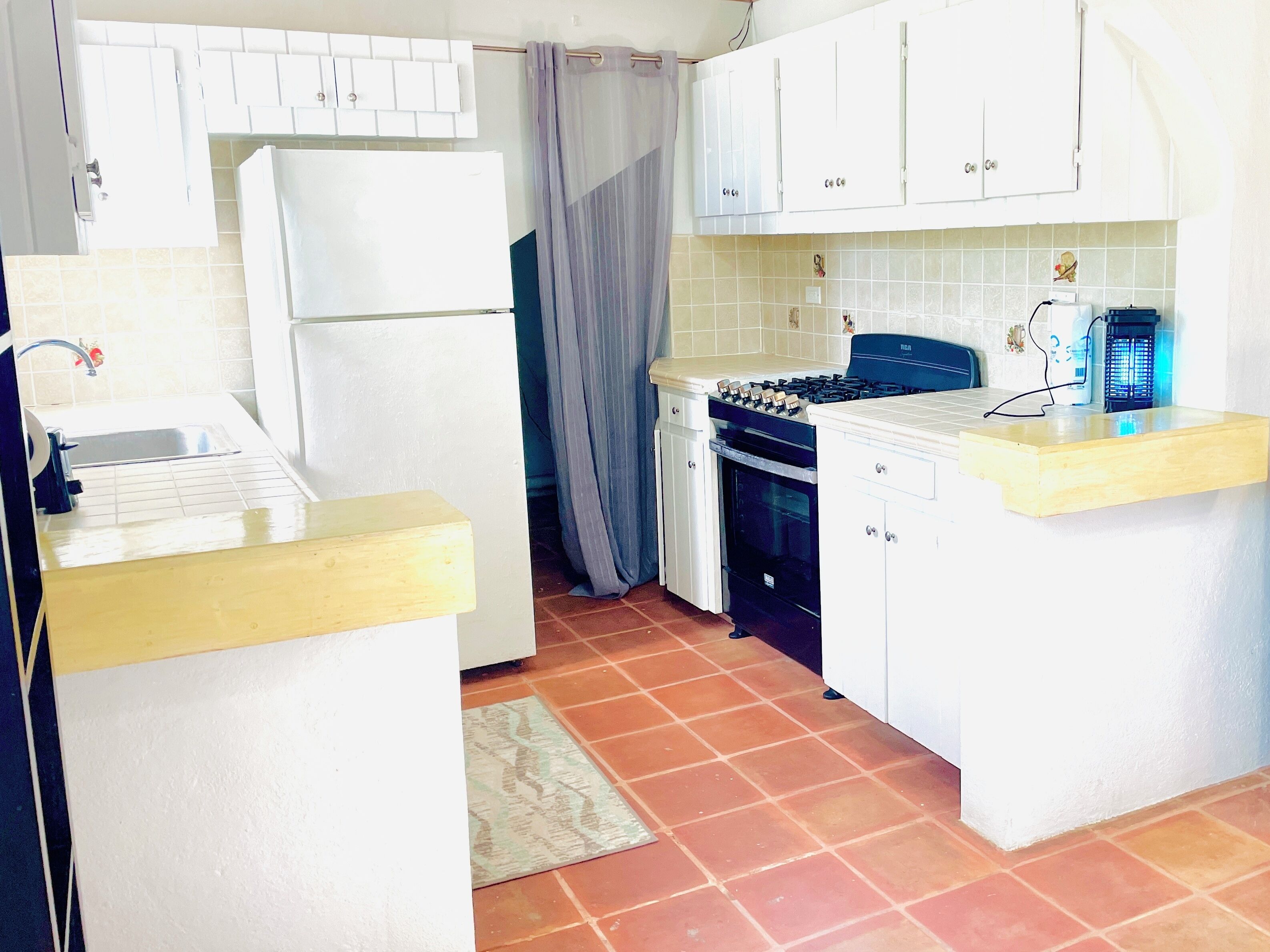 A compact kitchen with white cabinets, a refrigerator, a stove, and a sink.