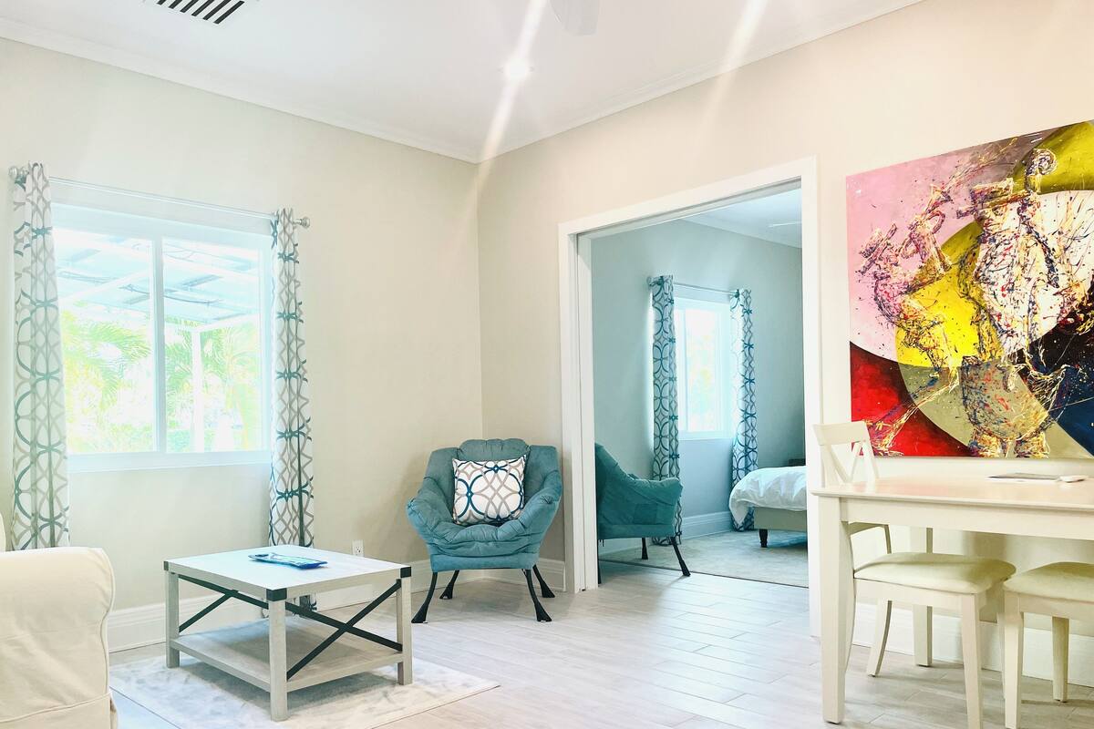 A modern living room with a teal armchair, a white coffee table, and a large abstract painting on the wall.