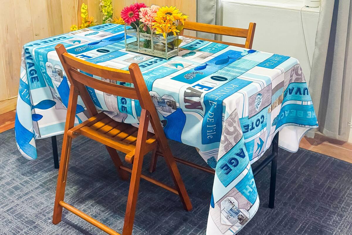 A dining table with a blue and white tablecloth, wooden chairs, and a vase with flowers.