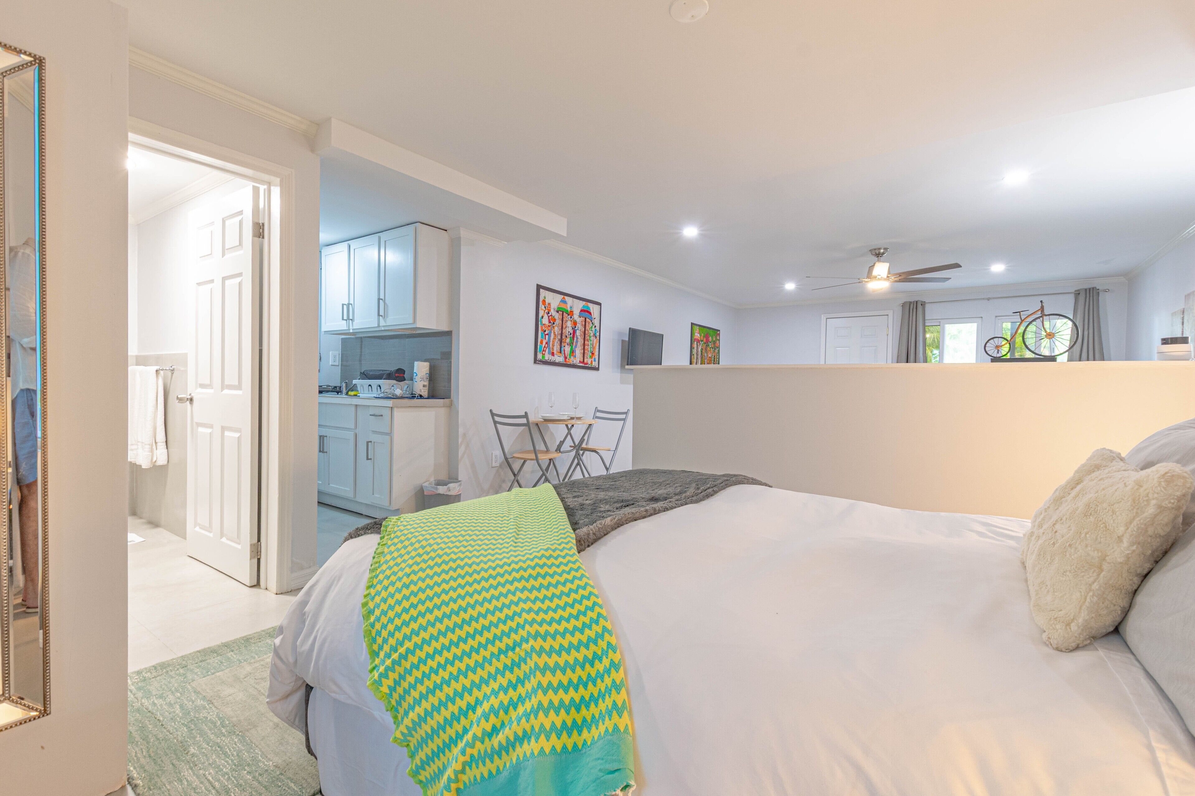 A bedroom with a bed, a green and yellow patterned blanket, a white pillow, and a ceiling fan.
