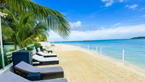 A beachside lounge with sun loungers, a palm tree, and a view of the ocean. - Blue Ocean Village (Nassau)