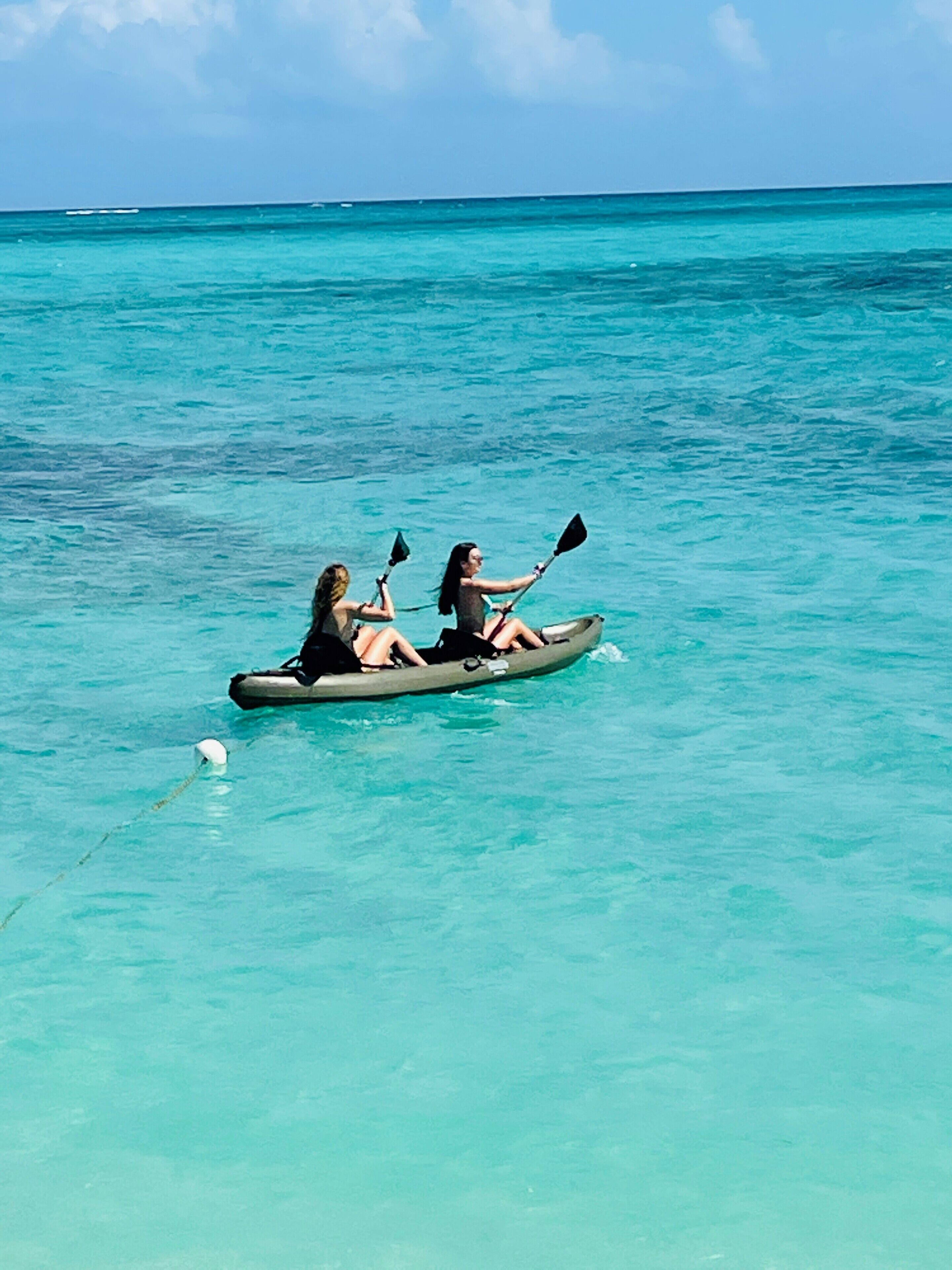 Deux personnes pratiquent le kayak sur une mer turquoise et calme.