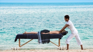 A massage therapy session on a beach with a wooden massage table and a towel. - Blue Ocean Village (Nassau)