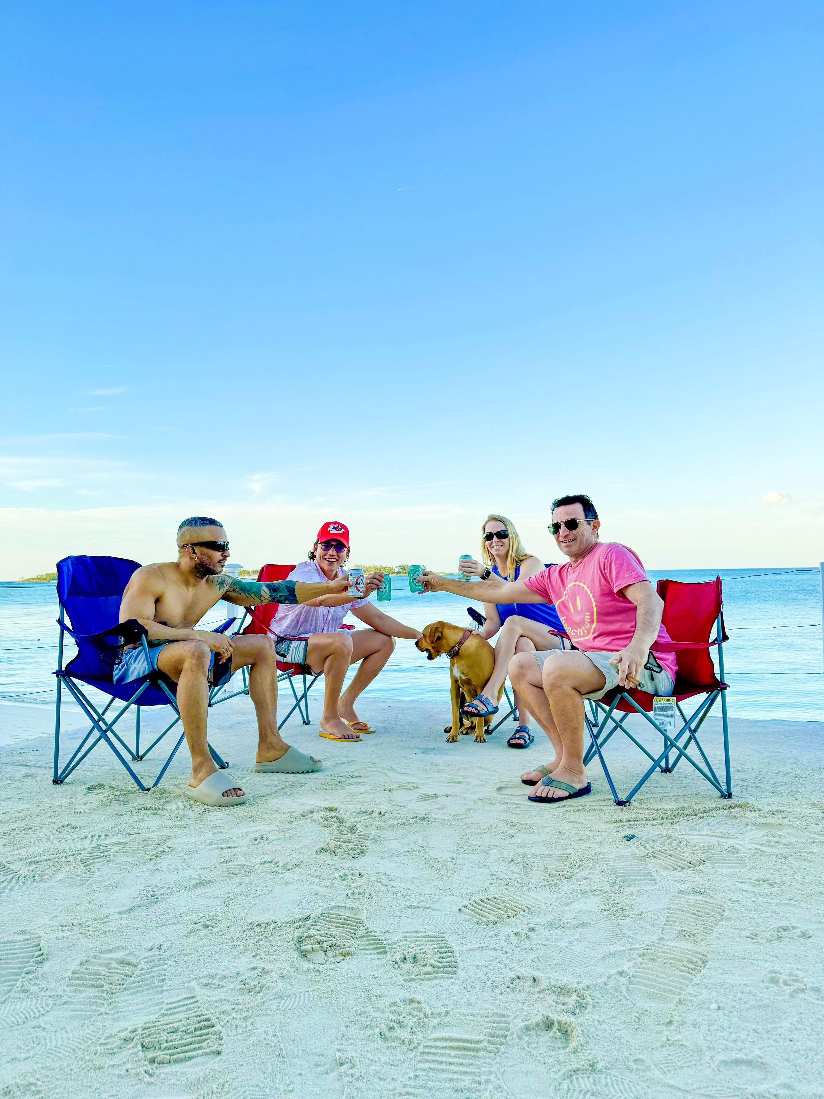 A group of people sitting on beach chairs on a sandy beach with a clear sky.