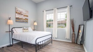 A bedroom with a bed, two bedside lamps, a painting, a window with curtains, a mirror, and a vase with branches. - Charming 3BR 2BA Gem Close to Downtown Riverwalk (San Antonio)