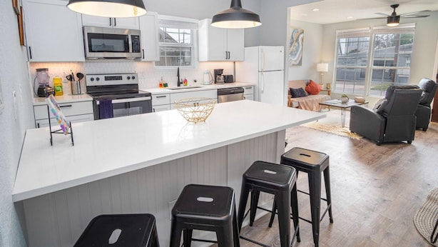 A modern kitchen with white cabinets, a central island with stools, and a dining area with a sofa and chairs. - Charming 3BR 2BA Gem Close to Downtown Riverwalk (San Antonio)