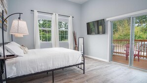 A bedroom with a bed, a nightstand, a lamp, a TV, and a sliding glass door to a balcony. - Charming 3BR 2BA Gem Close to Downtown Riverwalk (San Antonio)