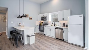 A modern kitchen with white cabinets, a stainless steel refrigerator, and a central island with bar stools. - Charming 3BR 2BA Gem Close to Downtown Riverwalk (San Antonio)