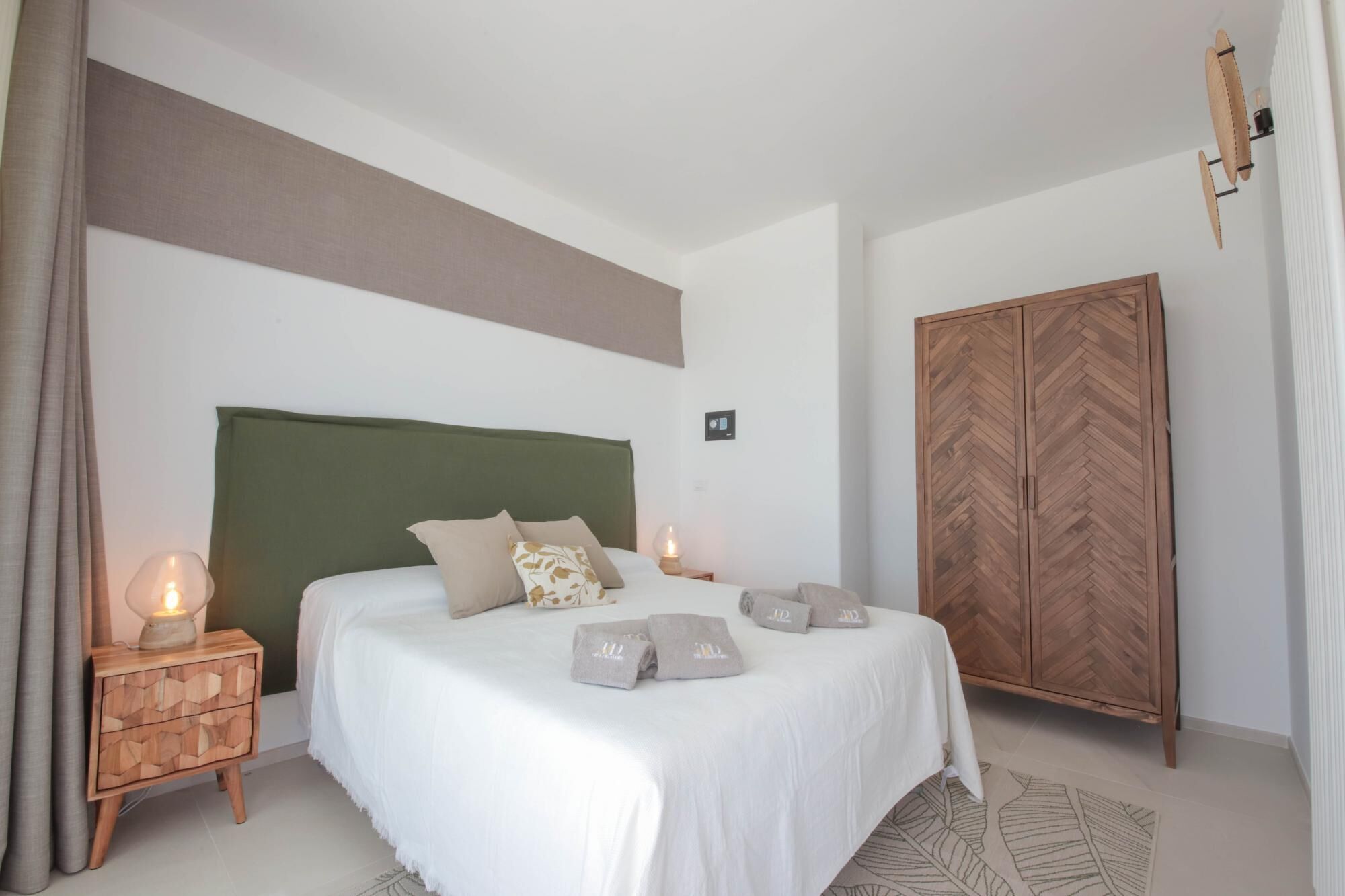 Ein Schlafzimmer mit Bett, Nachttischen, einem Kleiderschrank und einer Wandleuchte.