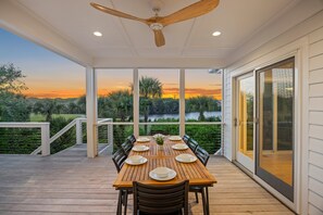 A covered outdoor dining area with a table set for six, a ceiling fan, and a view of a sunset over a body of water. - Luxurious Contemporary 4 BR Home, Golf Views! One Block to Beach! (Seabrook Island)