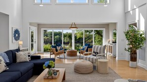 A spacious living area with a large window, a sofa, a coffee table, and a potted plant. - Luxurious Contemporary 4 BR Home, Golf Views! One Block to Beach! (Seabrook Island)