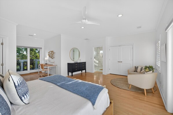 A bedroom with a bed, a desk, a dresser, a chair, a ceiling fan, and a view of the outdoors.