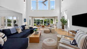 A spacious living room with a large TV, multiple seating areas, and large windows. - Luxurious Contemporary 4 BR Home, Golf Views! One Block to Beach! (Seabrook Island)