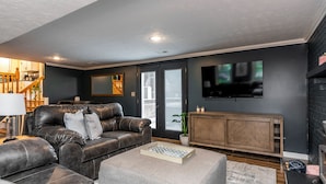 A modern living room with a dark gray wall, a leather sofa, a wooden cabinet, and a flat-screen TV mounted on the wall. - 3 BR 2 bath 5 beds! sleeps 8. Pool, hot tub oasis in LEX (Lexington)