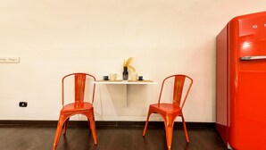 A small room with two orange chairs, a white table with a vase and cups, and a red refrigerator. - Via Duomo 196 in Naples (Naples)