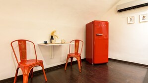 A room with a wooden floor, a white wall, and a red refrigerator. There are two red chairs and a small white table with a vase and cups. - Via Duomo 196 in Naples (Naples)