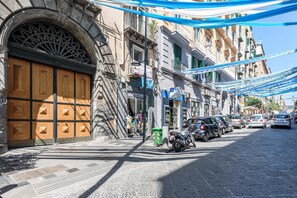 A cobblestone street with parked cars and a motorcycle, buildings with balconies, and a large wooden door. - Via Duomo 196 in Naples (Naples)
