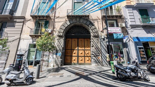 A street view with a prominent building featuring a large wooden door, a scooter parked in front, and a motorcycle parked on the sidewalk. - Via Duomo 196 in Naples (Naples)