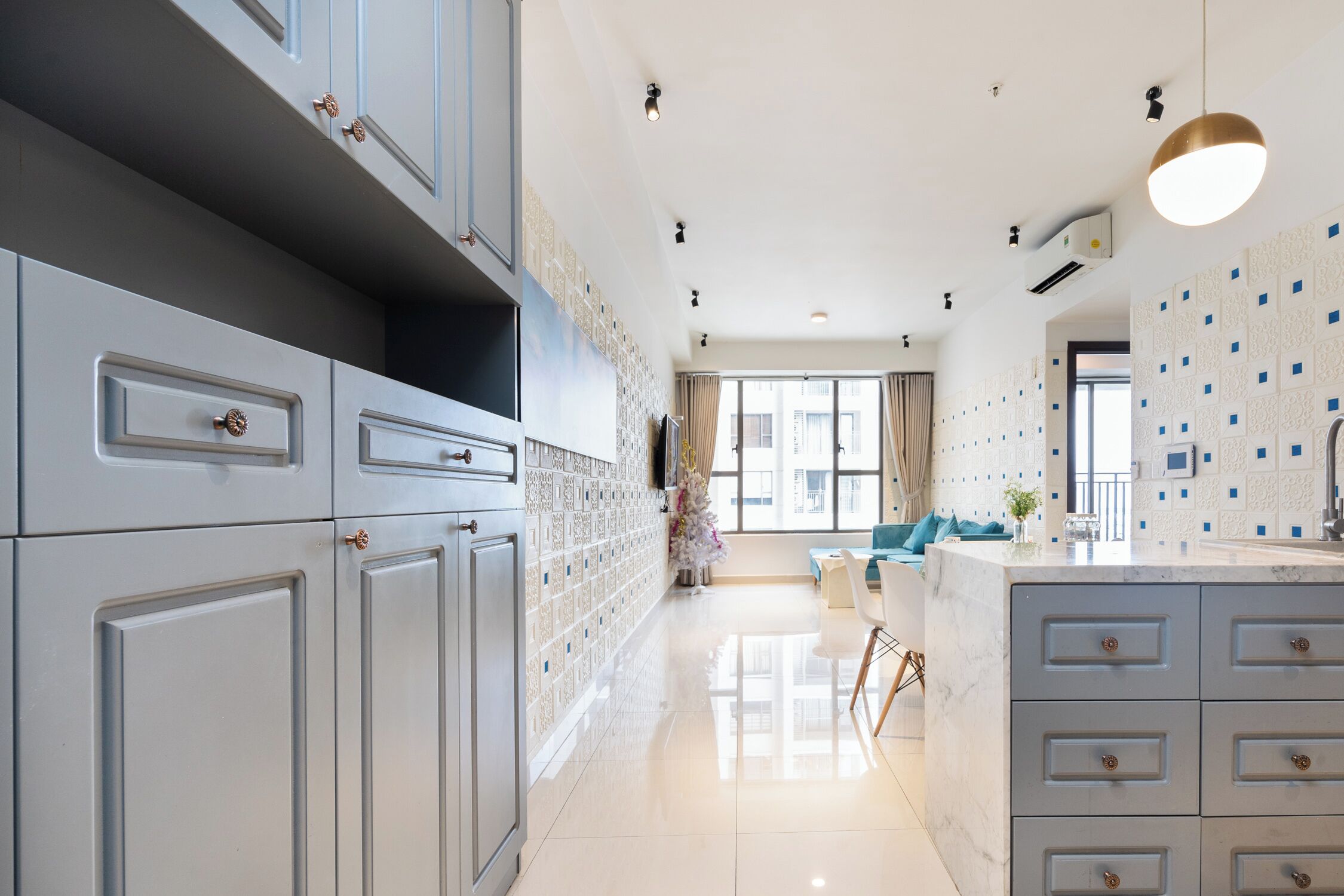 Une cuisine moderne avec des meubles gris, un îlot en marbre et des luminaires suspendus.