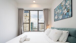 A hotel room with a large bed, white bedding, a teal headboard, and a city view through floor-to-ceiling windows. - Tresor 3 bedrooms with pool gym in center (Thành phố Hồ Chí Minh)