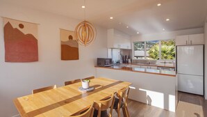 A modern kitchen with white cabinets, a wooden island, and a dining area with a wooden table and chairs. - Tahuna Beach Oasis - Home in the heart of Tahunanui Beach recreational paradise (Nelson)