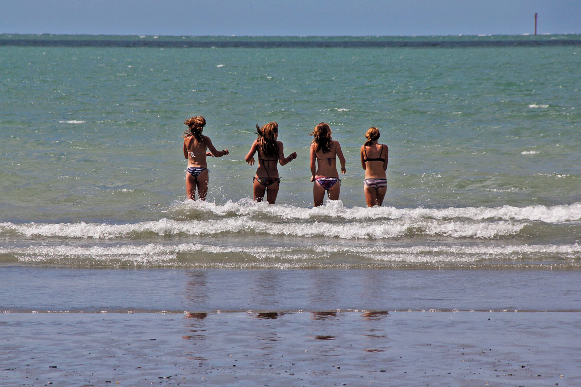 Escena de playa con cuatro personas en traje de baño de pie en aguas poco profundas.