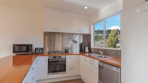 A modern kitchen with white cabinets, a wooden countertop, a built-in oven, a microwave, a coffee maker, and a dishwasher. - Tahuna Beach Oasis - Home in the heart of Tahunanui Beach recreational paradise (Nelson)