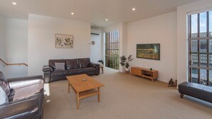 A spacious living room with a leather sofa, a wooden coffee table, and a large window with a view of the city. - Tahuna Beach Oasis - Home in the heart of Tahunanui Beach recreational paradise (Nelson)