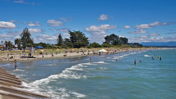 A beach with waves, people, and umbrellas. - Tahuna Beach Oasis - Home in the heart of Tahunanui Beach recreational paradise (Nelson)
