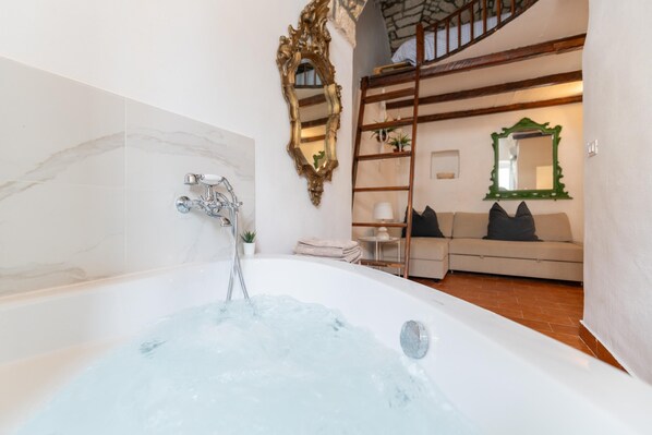 A bathroom with a bathtub, a wooden ladder, a sofa, and a mirror.