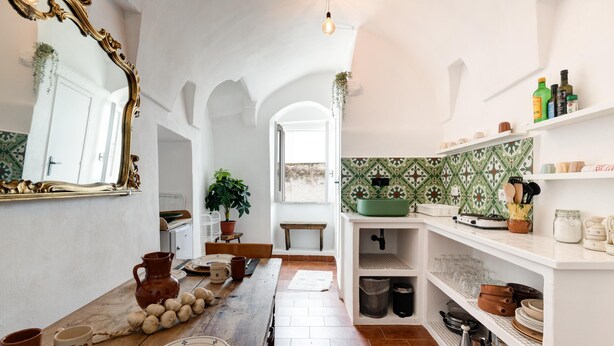 A kitchen with a rustic wooden table, a large ornate mirror, and shelves with kitchenware. - Biancostuni 44, The Little White Houses (Ostuni)