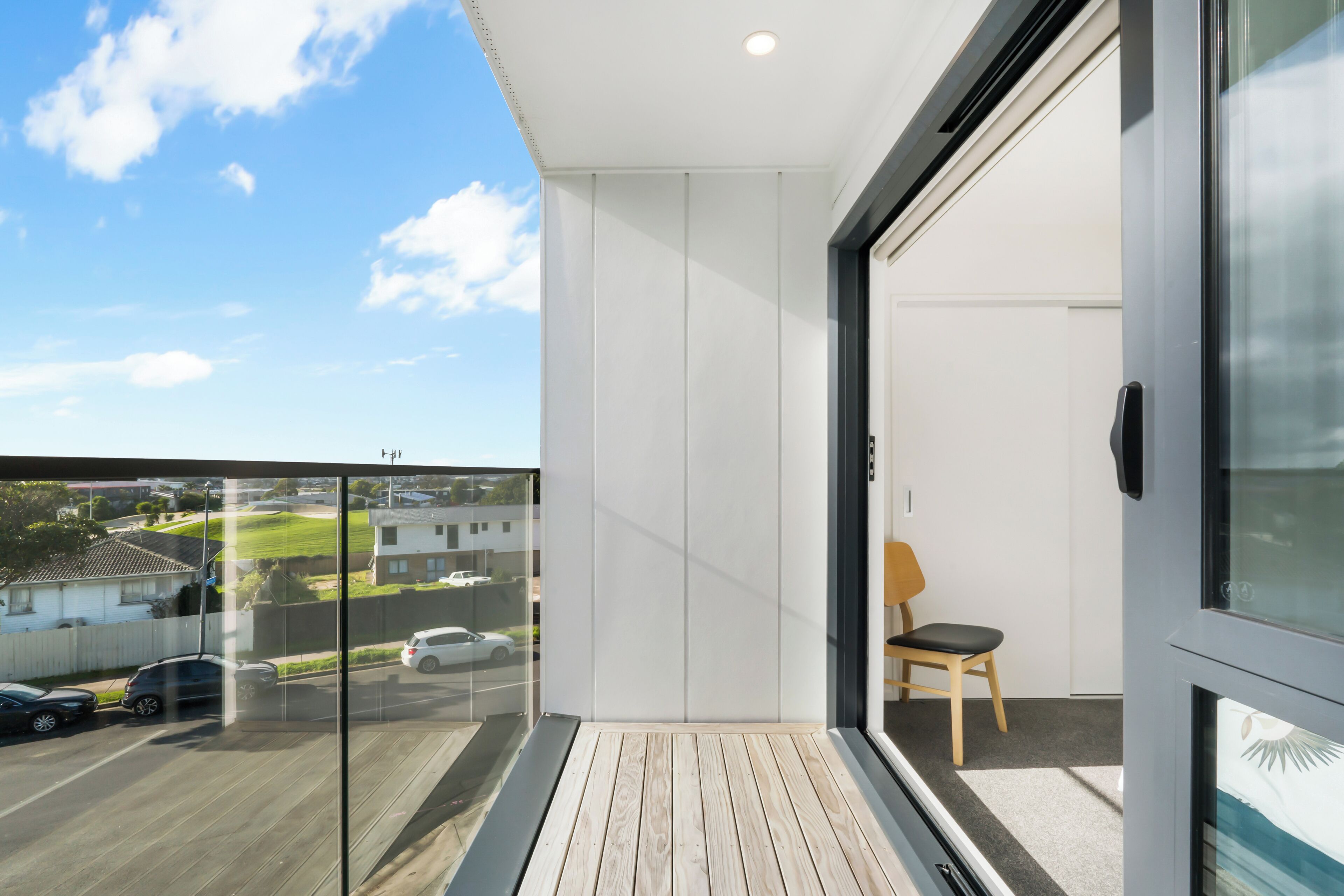 A modern balcony with a wooden floor, a glass door, and a view of a residential street.