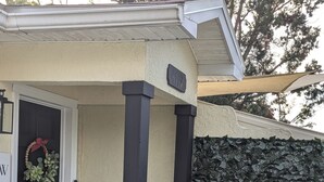 L'ingresso di una casa con una porta scura, un cartello di benvenuto, una ghirlanda, una pianta in vaso, un lanternino e un muro in pietra.