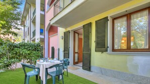 Un balcon avec une table et des chaises, une porte et une fenêtre avec des volets.