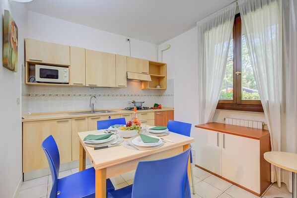 Une cuisine moderne avec des meubles en bois, un four à micro-ondes et un coin repas avec des chaises bleues et une table dressée pour deux personnes.