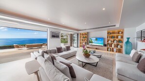 A modern living room with a large TV, comfortable seating, and a view of the ocean. - Villa La Prana (Kamala)