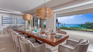 A dining area with a wooden table set for six, surrounded by wicker chairs, with a view of the ocean. - Villa La Prana (Kamala)