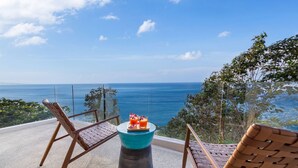 Un balcone con sedie in vimini e un tavolo con bevande, vista su un mare cristallino e azzurro.