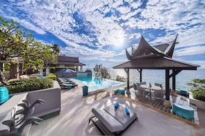 A luxurious outdoor pool area with lounge chairs, a covered seating area, and a view of the sea.