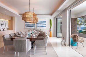 A modern dining area with a large table set for six, surrounded by wicker chairs. - Villa La Prana (Kamala)