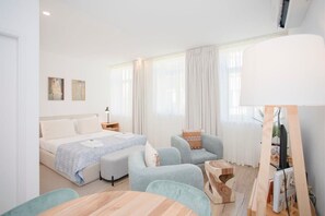 A modern hotel room with a bed, two armchairs, a wooden coffee table, and a desk with a lamp. - Liiiving in Porto - Urban Art Apartment (Porto)