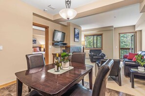 A modern living room with a dark wooden dining table, leather chairs, a sofa, and a TV. - Spacious King Bed with Pool & Hot Tubs (Canmore)