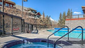 A hot tub with a tiled edge, a pool, and a view of a mountain in the background. - Spacious King Bed with Pool & Hot Tubs (Canmore)