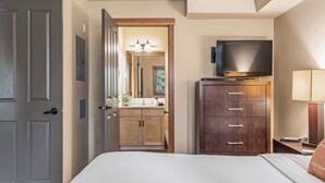 A hotel room with a bed, a TV on a wooden cabinet, a bathroom with a mirror, and a door. - Spacious King Bed with Pool & Hot Tubs (Canmore)