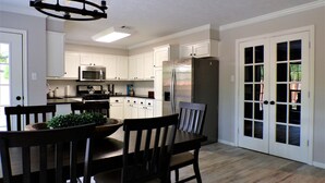 A modern kitchen with white cabinets, a stainless steel refrigerator, and a dining area with a wooden table and chairs. - Backyard Oasis with Private Pool, SPA and Putting Green only 2 Miles from TAMU! (College Station)