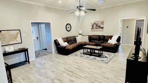 A spacious living room with a large sectional sofa, a coffee table, and a ceiling fan. - Backyard Oasis with Private Pool, SPA and Putting Green only 2 Miles from TAMU! (College Station)